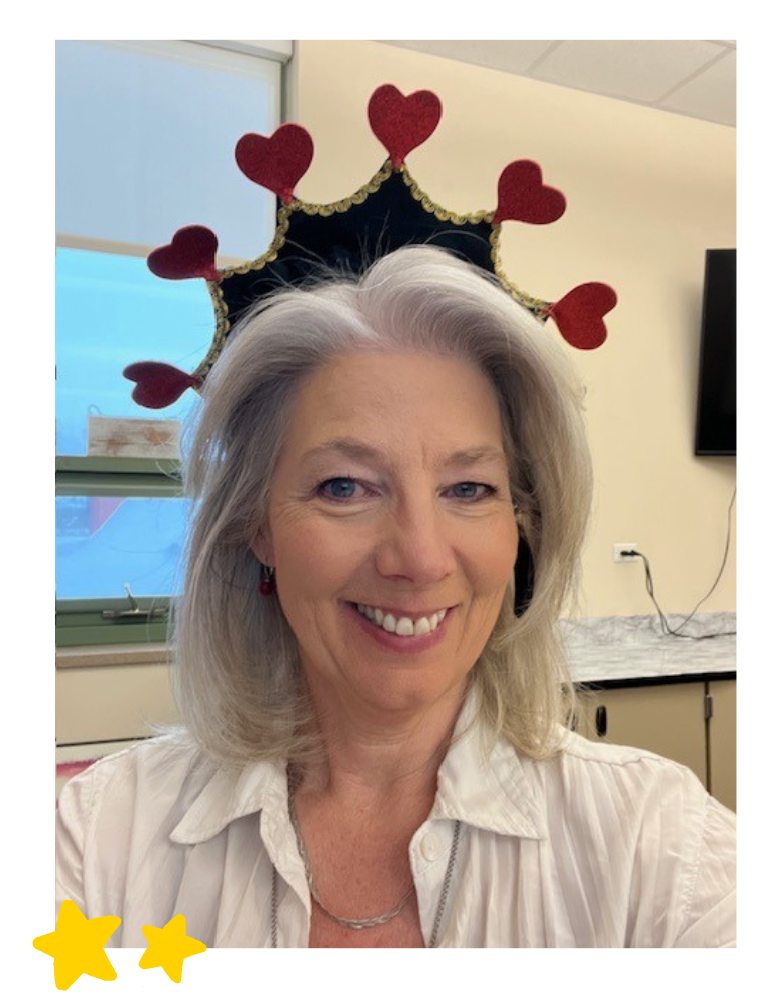 A portrait of Shelley Smith, a woman with grey hair and a warm smile, wearing a white button-down shirt and a black headband crowned with red glittery hearts. Two bright yellow hand-drawn stars are positioned in the bottom-left corner of the white border surrounding the photo.