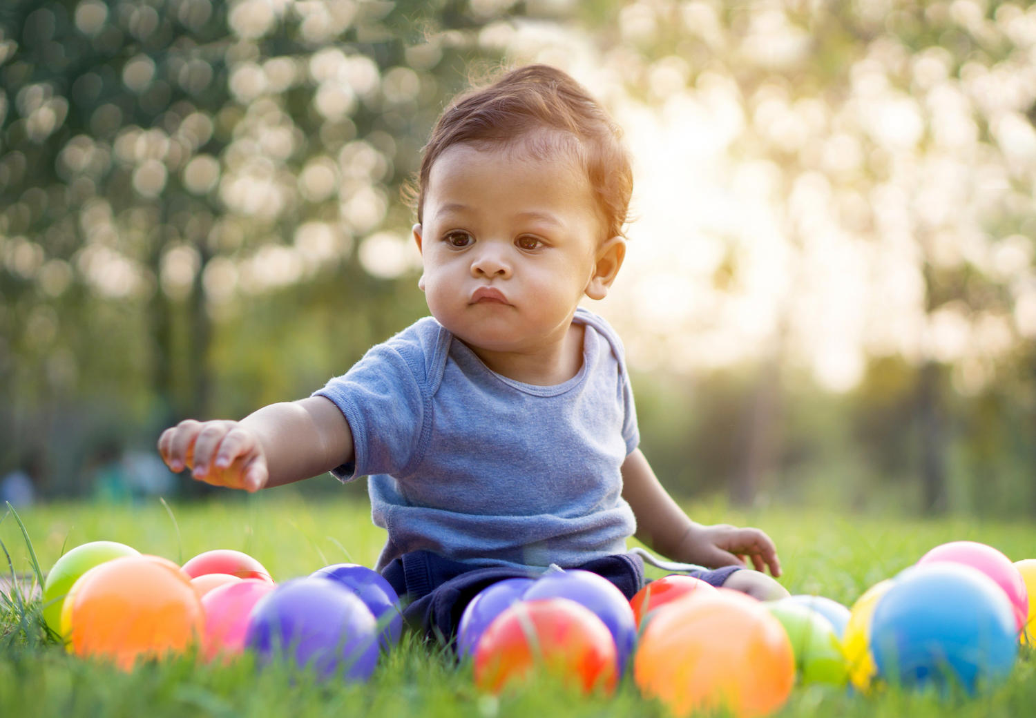 Baby playing outside in green grass with multicolored balls.