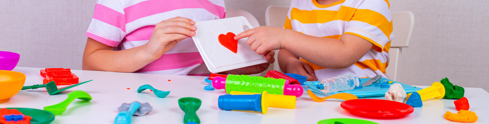 Two children of preschool age playing with colorful toys and one pointing to a red heart.